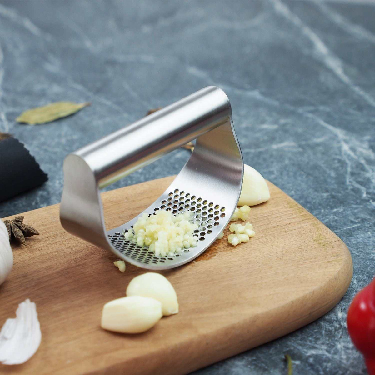 Stainless steel best garlic crusher garlic press rocker with finely minced garlic on wooden board and whole garlic cloves beside it