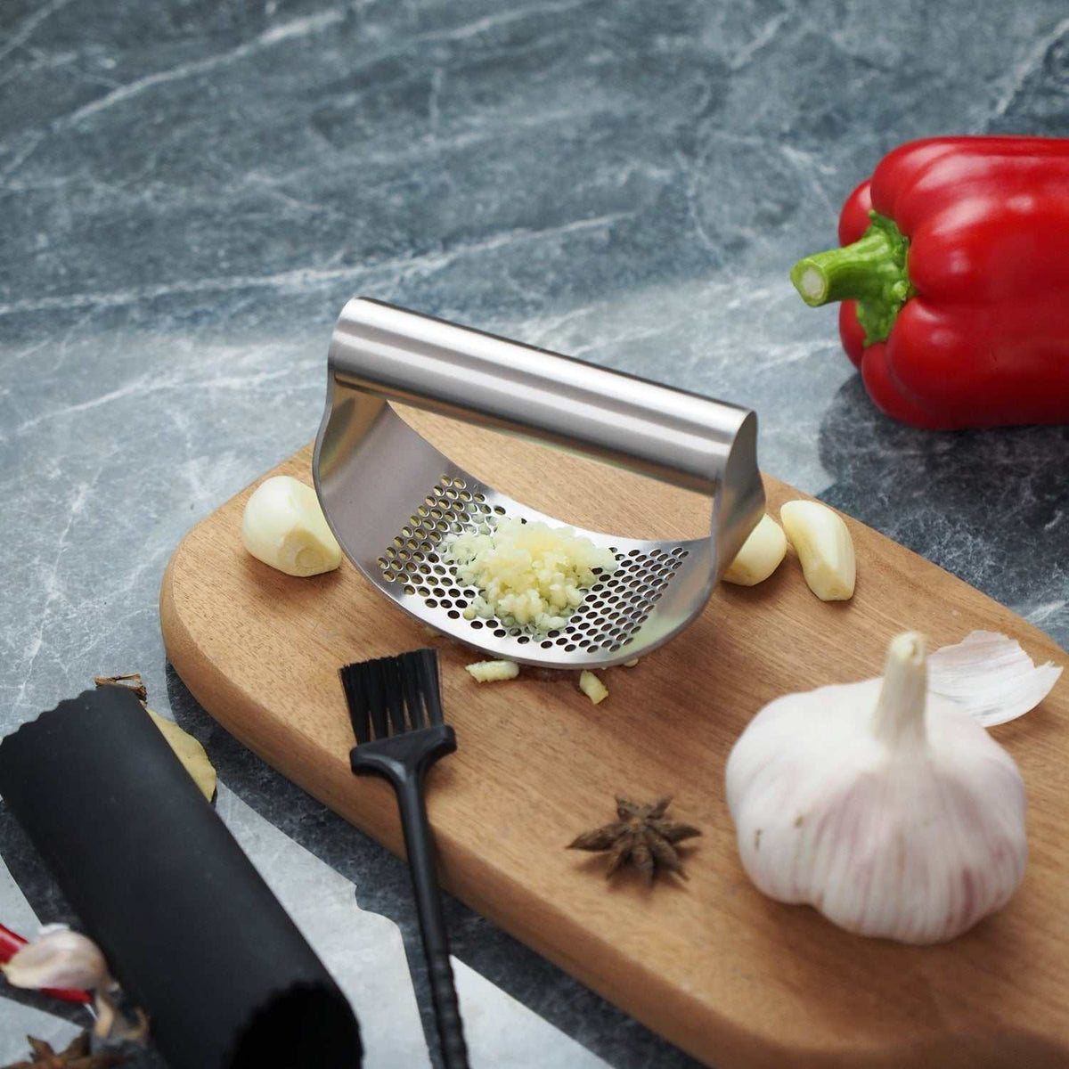 Best garlic crusher stainless steel rocker with finely minced garlic on wooden board near garlic cloves and red pepper