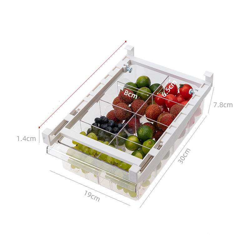 Under-Shelf Pull-Out clear plastic fridge drawer organizer with white frame, divided compartments holding various fruits like tomatoes, grapes, and limes, with measurement markings on sides.